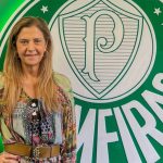Leila Pereira posa sorridente em frente a logo do Palmeiras.