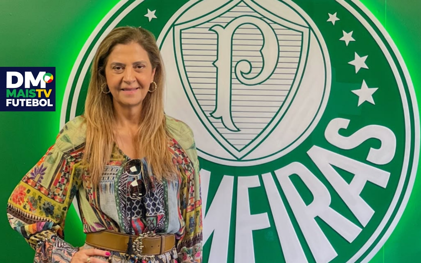 Leila Pereira posa sorridente em frente a logo do Palmeiras.